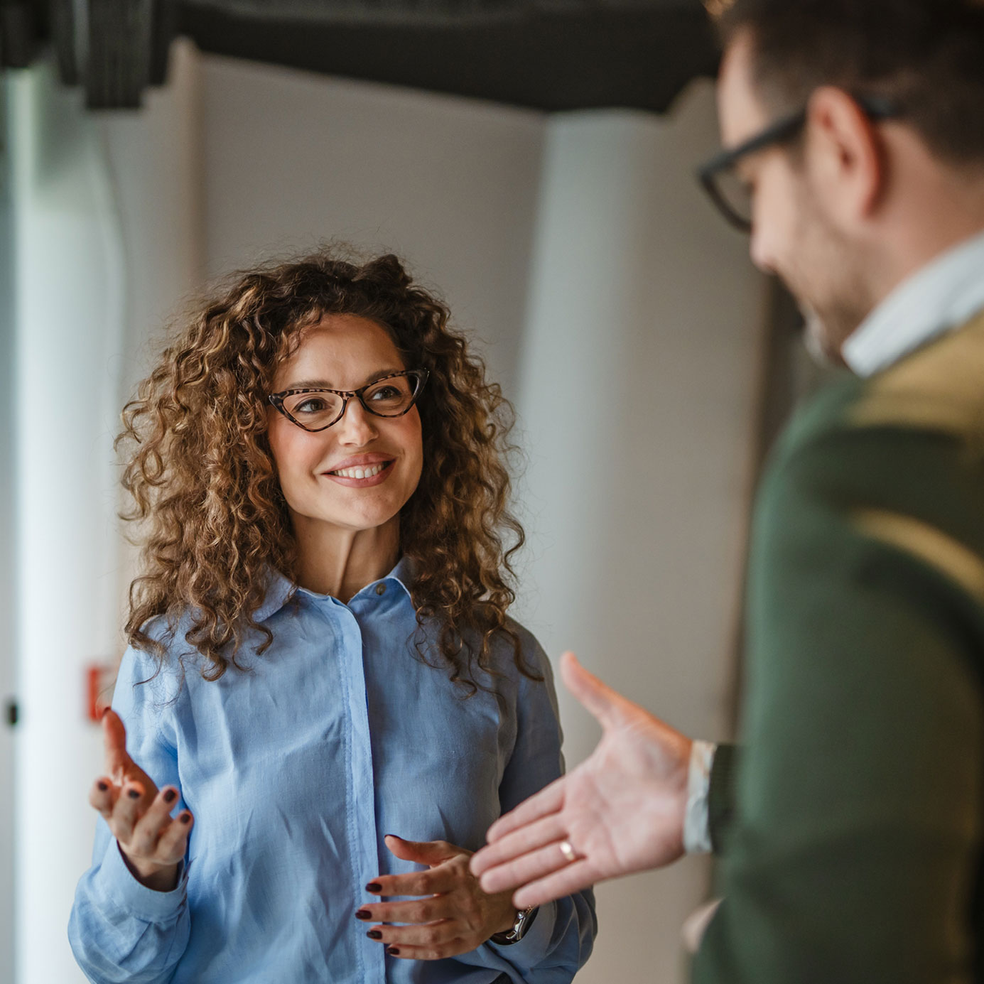 Person mit lockigen Haaren in hellblauer Bluse gestikuliert mit einer weiteren Person im Vordergrund
