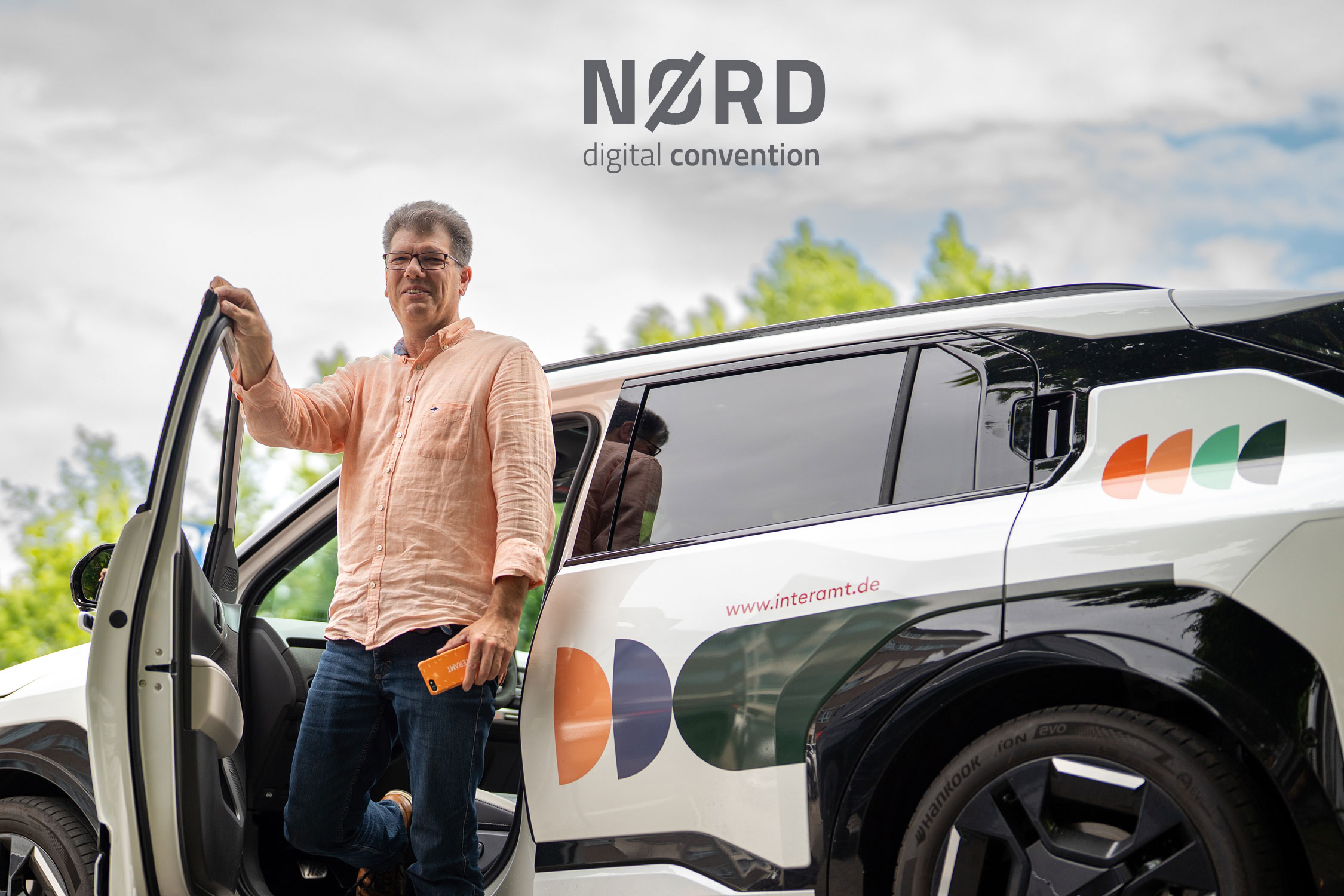Person stepping out of a white car with colorful patterns and the text 'www.interamt.de' on the side, with the words 'NØRD digital convention' above