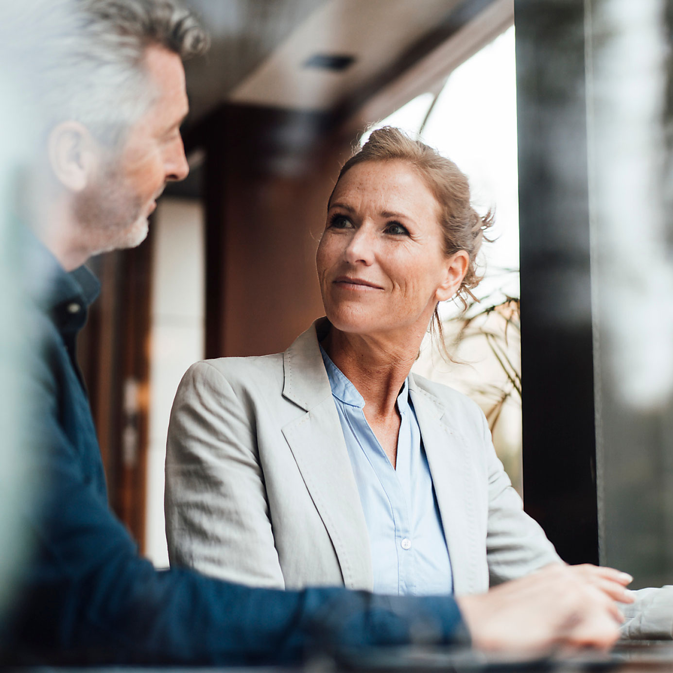 Person in hellem Blazer sitzt an einem Tisch und hält die Hände vor sich