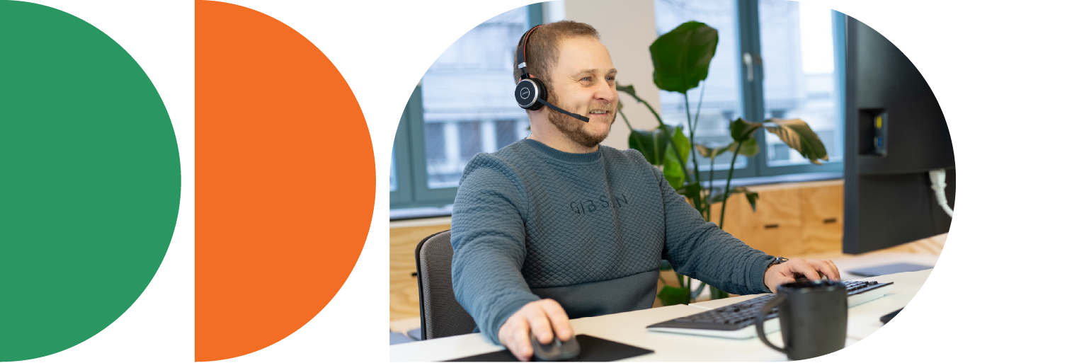 Mann mit Headset sitzt vor einem Computer in einem hellen Büroraum und führt ein Service-Telefonat.